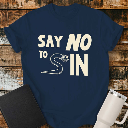 true navy T-shirt featuring bold black typography reading “SAY NO TO SIN,” with a smiling cartoon snake cleverly forming the letter “S” in “SIN.” The shirt is displayed on a rustic wood plank background alongside a black Bible and a white insulated tumbler.