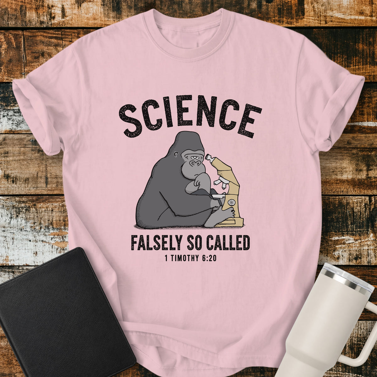 blossom pink Christian t-shirt featuring a gorilla examining a microscope beneath the word “Science,” with “Falsely So Called” and 1 Timothy 6:20 below. A clever retro-inspired biblical design referencing the KJV warning against “oppositions of science falsely so called.”