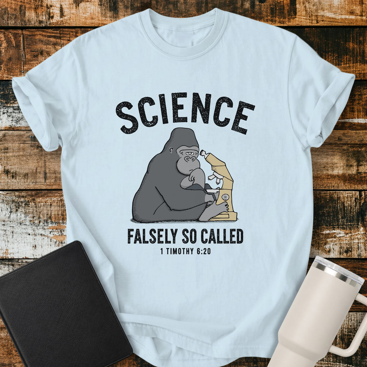 chambray blue Christian t-shirt featuring a gorilla examining a microscope beneath the word “Science,” with “Falsely So Called” and 1 Timothy 6:20 below. A clever retro-inspired biblical design referencing the KJV warning against “oppositions of science falsely so called.”