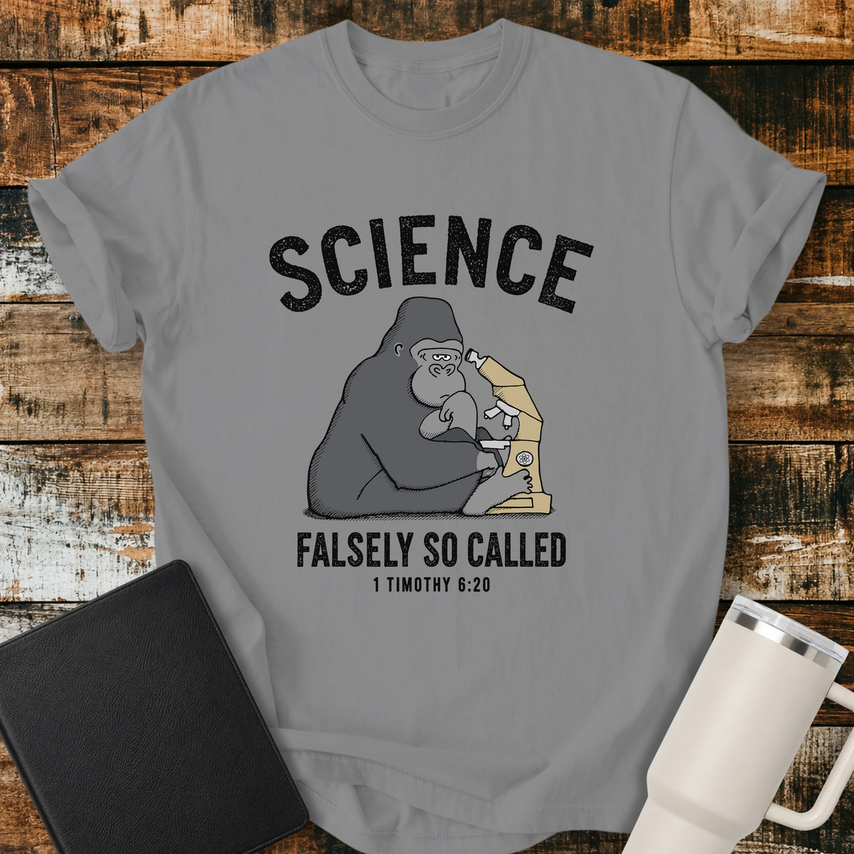 grey Christian t-shirt featuring a gorilla examining a microscope beneath the word “Science,” with “Falsely So Called” and 1 Timothy 6:20 below. A clever retro-inspired biblical design referencing the KJV warning against “oppositions of science falsely so called.”