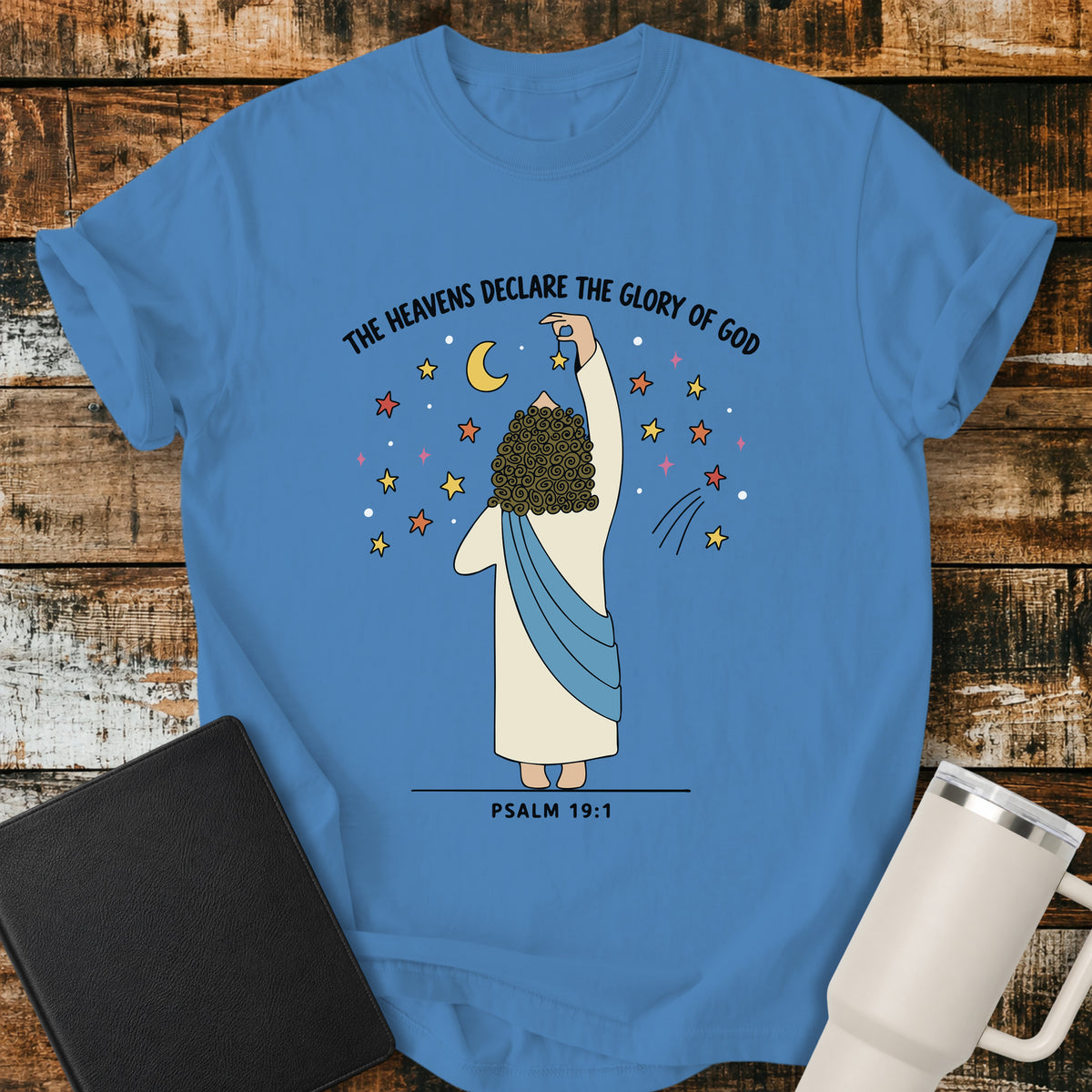 royal caribe blue Christian t-shirt featuring a whimsical illustration of God placing stars in the heavens, with the text “The Heavens Declare the Glory of God” and Psalm 19:1.