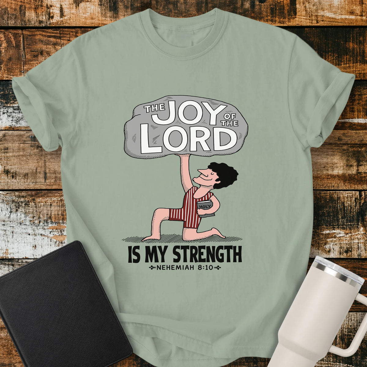 bay green Christian t-shirt featuring a vintage-style illustration of a man lifting a large stone reading “The Joy of the Lord,” with the words “Is My Strength” and Nehemiah 8:10 below.