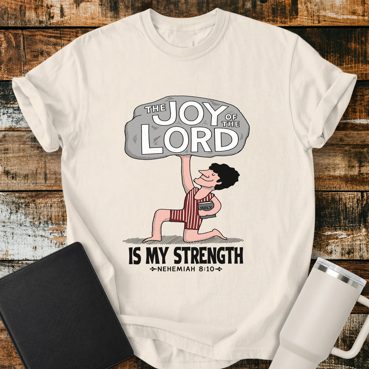 Ivory Christian t-shirt featuring a vintage-style illustration of a man lifting a large stone reading “The Joy of the Lord,” with the words “Is My Strength” and Nehemiah 8:10 below.
