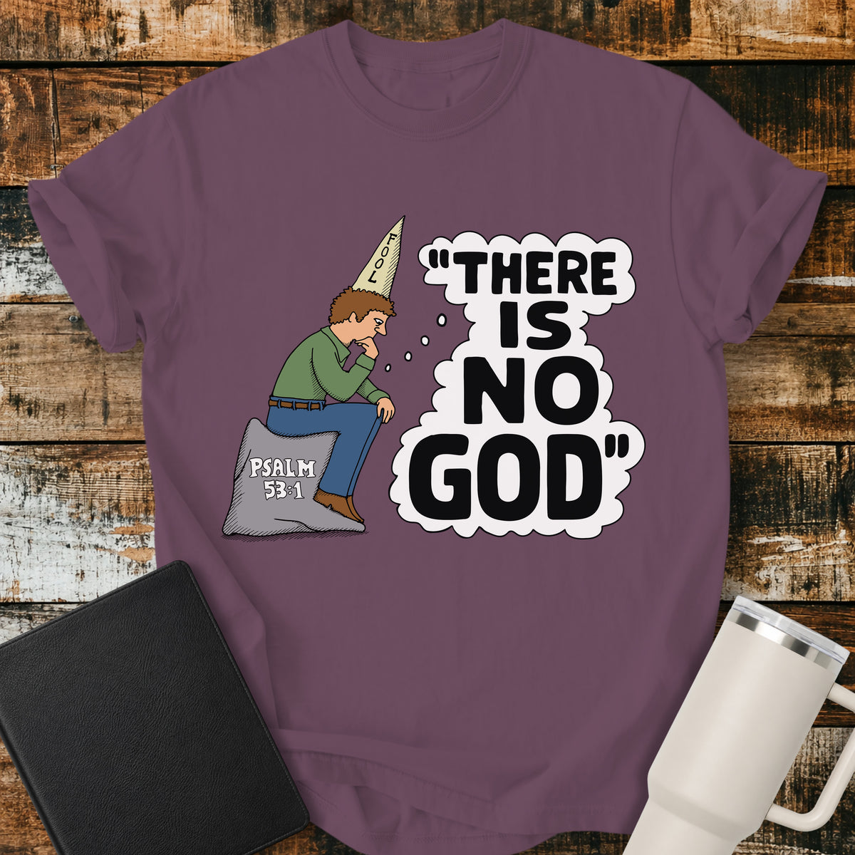 berry purple Christian t-shirt featuring a humorous illustration of a man in a “FOOL” cap pondering the statement “There Is No God,” inspired by Psalm 53:1.