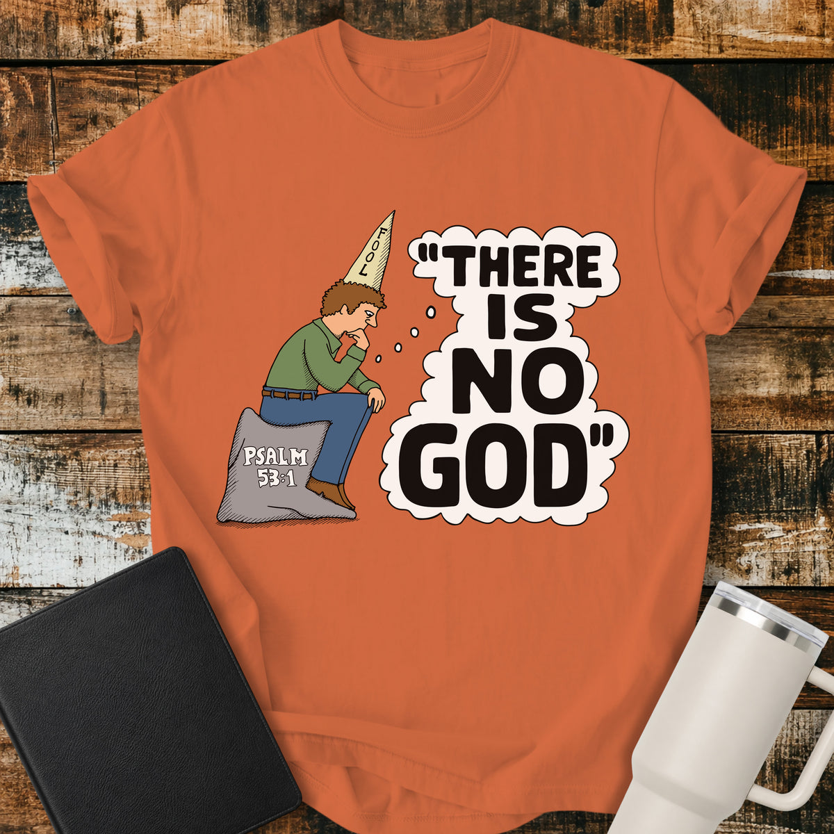 burnt orange Christian t-shirt featuring a humorous illustration of a man in a “FOOL” cap pondering the statement “There Is No God,” inspired by Psalm 53:1.