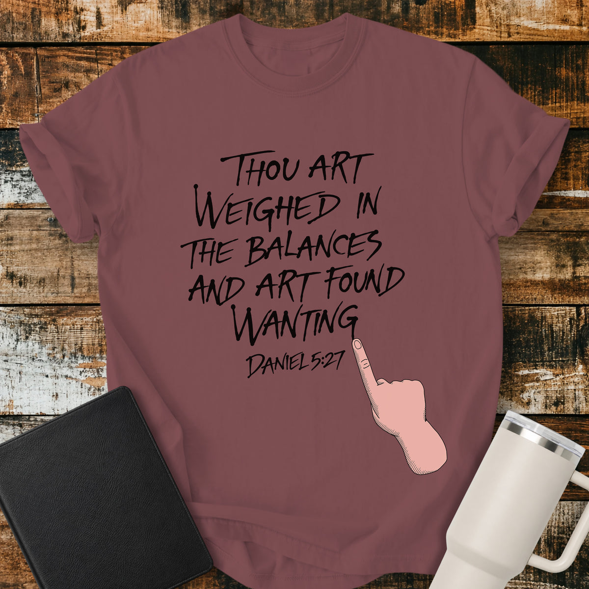 brick red Christian t-shirt featuring hand-lettered typography with Daniel 5:27: “Thou art weighed in the balances, and art found wanting,” paired with a pointing-hand illustration.