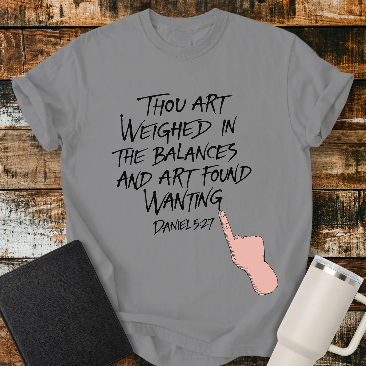 grey Christian t-shirt featuring hand-lettered typography with Daniel 5:27: “Thou art weighed in the balances, and art found wanting,” paired with a pointing-hand illustration.