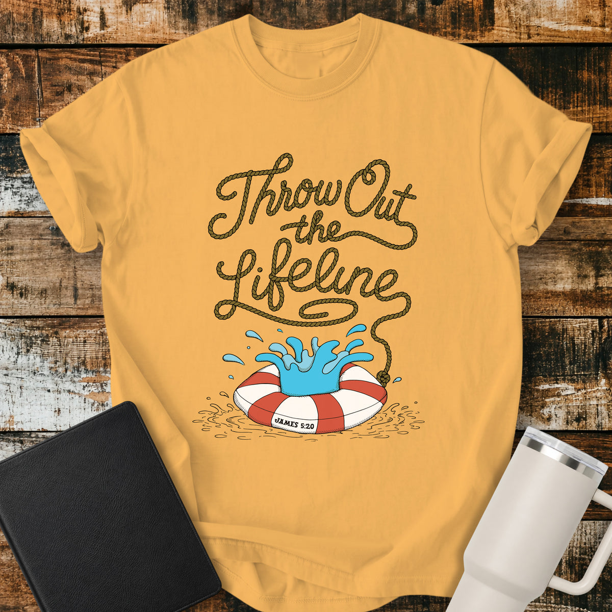 citrus yellow flat-lay t-shirt mockup featuring rope-style lettering that reads, “THROW OUT THE LIFELINE,” flowing down into a red-and-white life preserver splashing in water. The design includes the Bible reference “James 5:20.” The shirt is displayed on a rustic wood plank background alongside a black leather Bible and a white insulated travel mug.