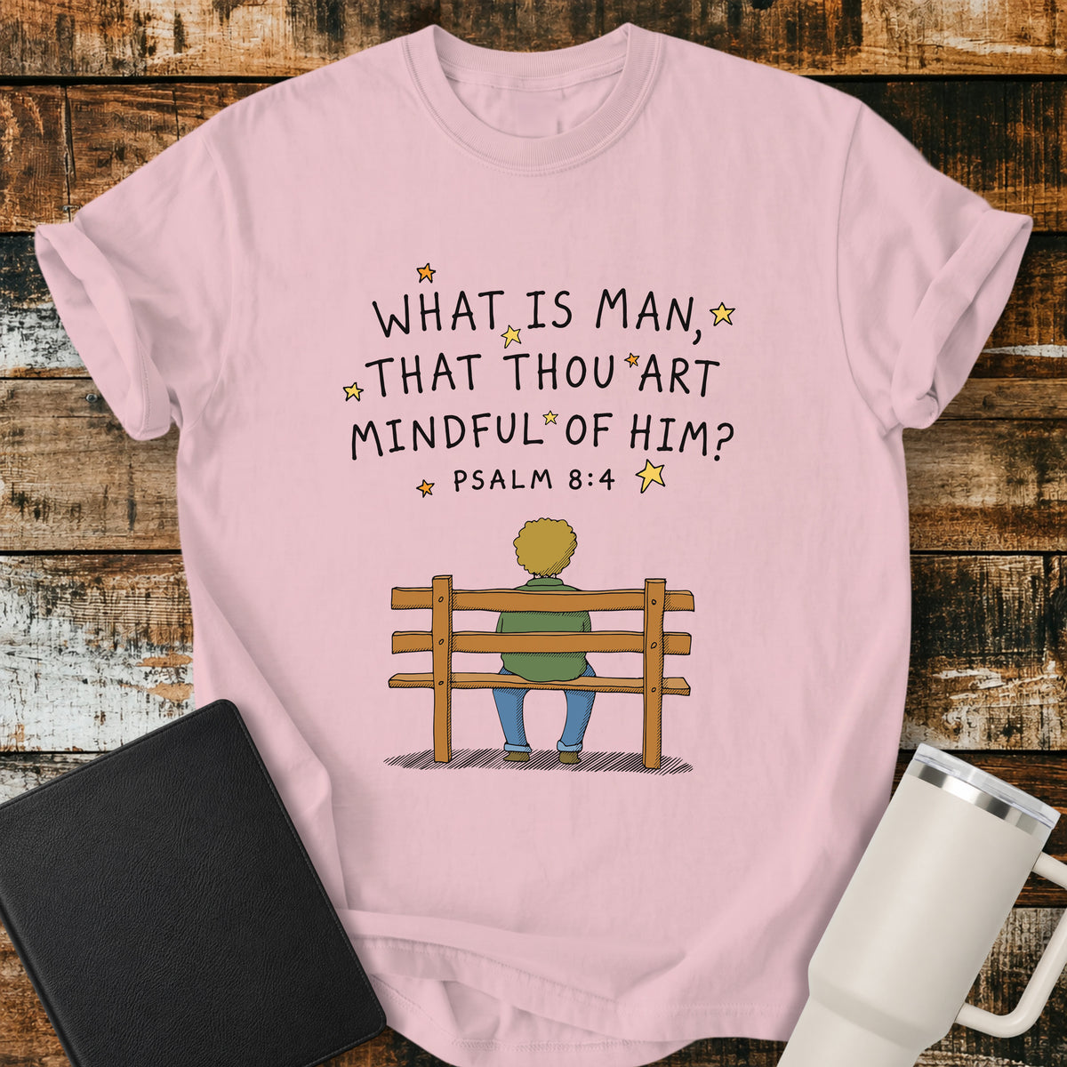 blossom pink Christian t-shirt featuring the words “What Is Man, That Thou Art Mindful of Him?” from Psalm 8:4, surrounded by simple stars above a person sitting quietly on a wooden bench. A reflective, vintage-inspired biblical design centered on God’s care for mankind.