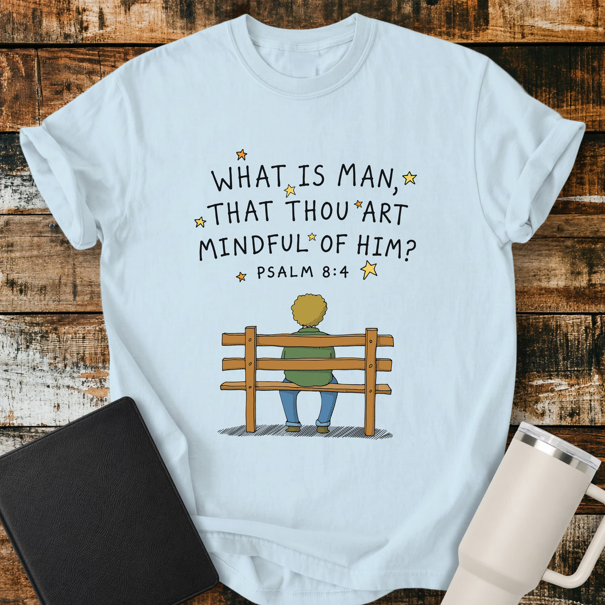 Chambray blue Christian t-shirt featuring the words “What Is Man, That Thou Art Mindful of Him?” from Psalm 8:4, surrounded by simple stars above a person sitting quietly on a wooden bench. A reflective, vintage-inspired biblical design centered on God’s care for mankind.
