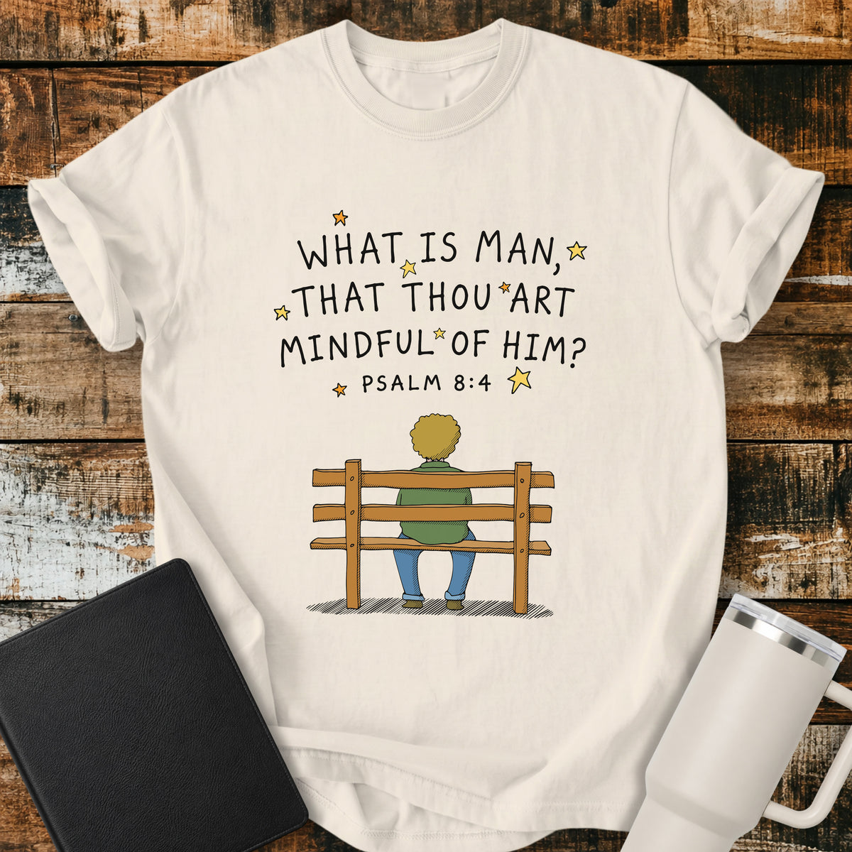 ivory Christian t-shirt featuring the words “What Is Man, That Thou Art Mindful of Him?” from Psalm 8:4, surrounded by simple stars above a person sitting quietly on a wooden bench. A reflective, vintage-inspired biblical design centered on God’s care for mankind.