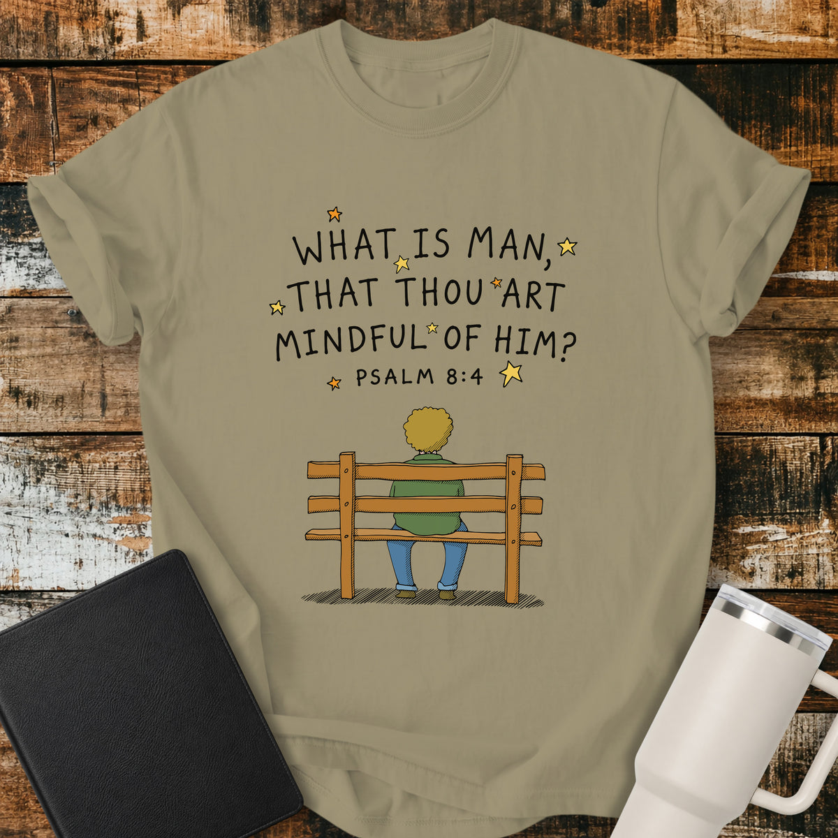 khaki Christian t-shirt featuring the words “What Is Man, That Thou Art Mindful of Him?” from Psalm 8:4, surrounded by simple stars above a person sitting quietly on a wooden bench. A reflective, vintage-inspired biblical design centered on God’s care for mankind.